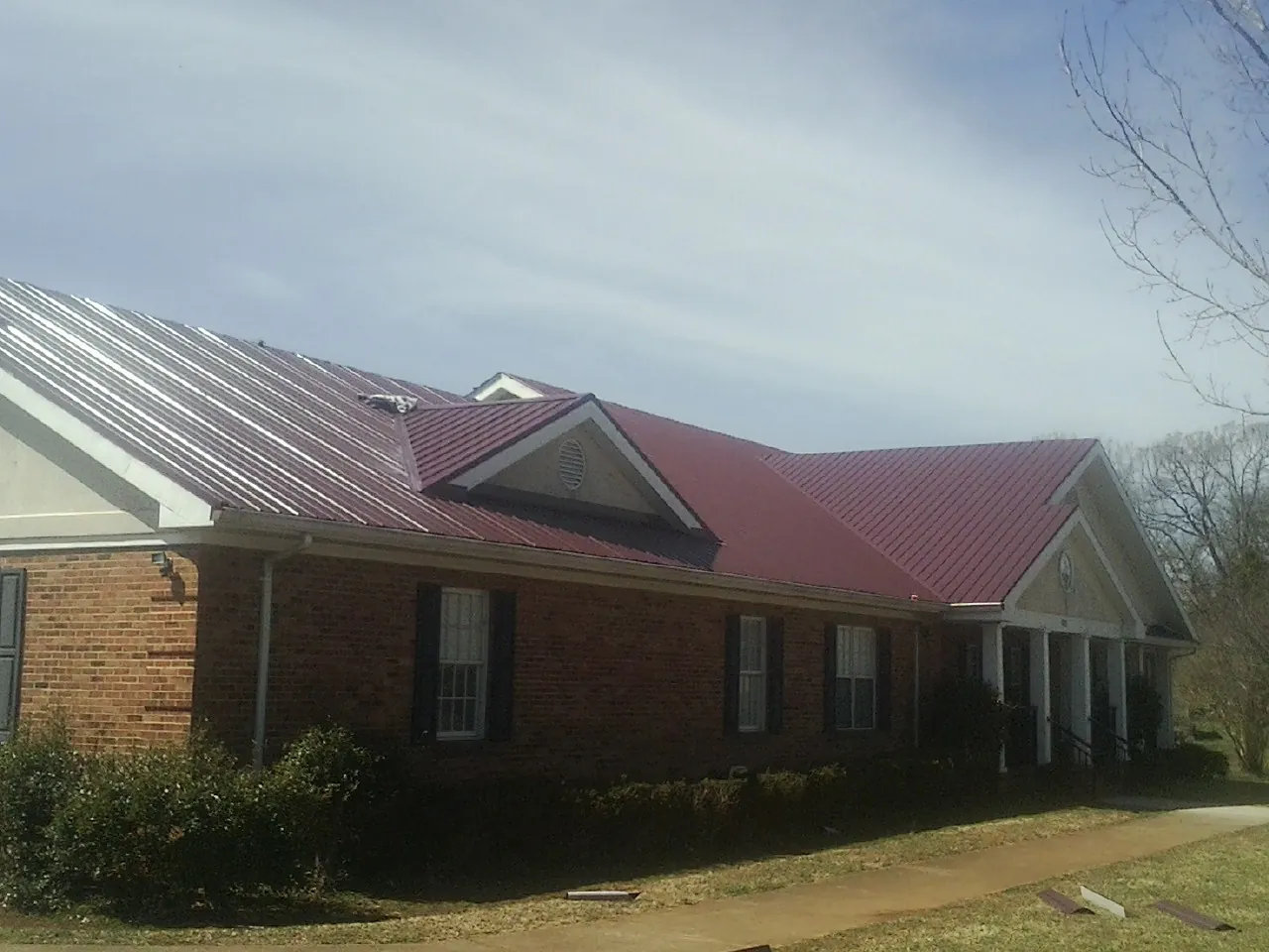 Red metal roof with gabled entries on a long brick building, from a Hail Damage Roof Repair job in Patrick