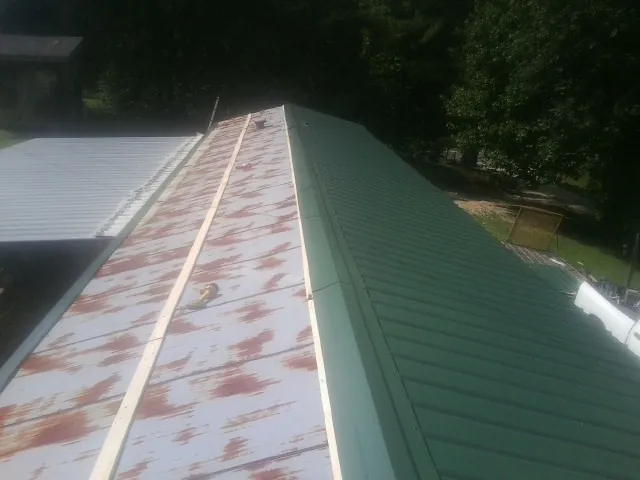 Old rusted panels beside newly installed green metal roofing — Wind Damage Roof Repair by Roofing Brothers in Patrick